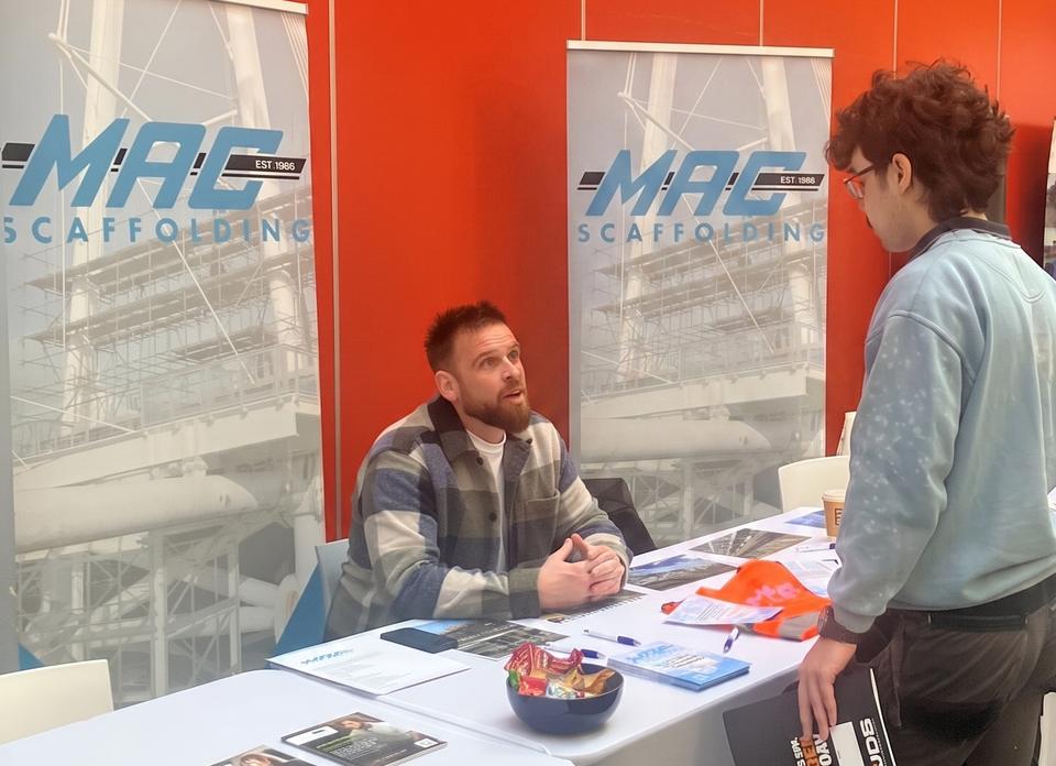 Jermain talking with a visitor across the MAC Scaffolding stand at an apprenticeship fair