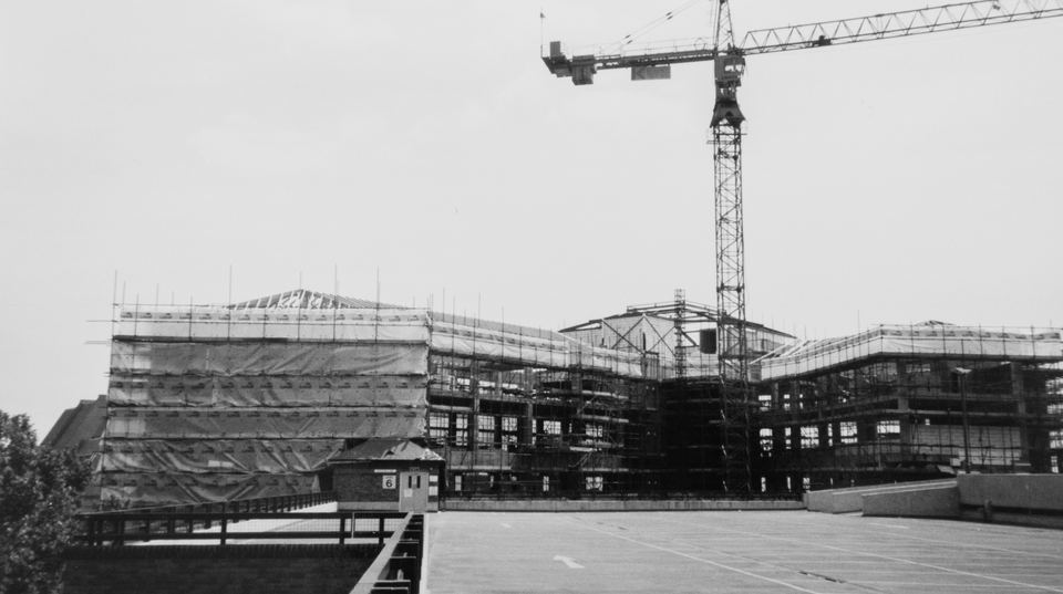 An early MAC Scaffolding contract: a steel frame under construction beneath a tower crane, photographed in black and white