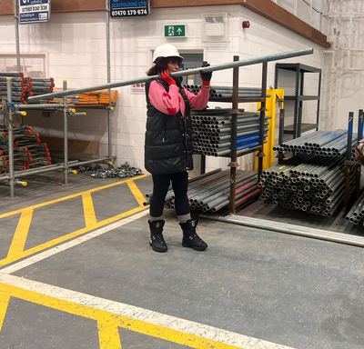 Sarah-Jayne Parsons in a hard hat beside the scaffold racks in the MAC yard