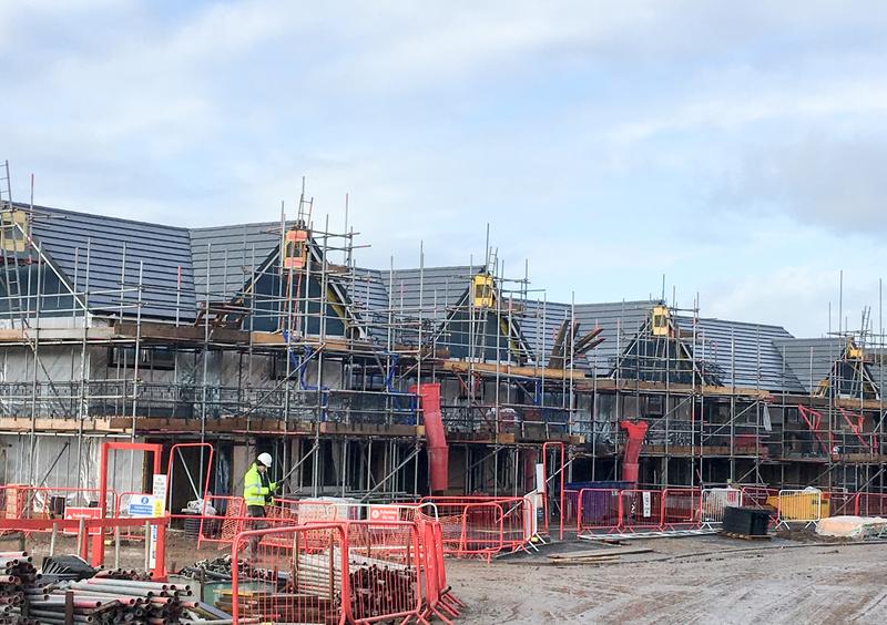 A terrace of new-build houses under a full access scaffold, their slate roofs part-sheeted
